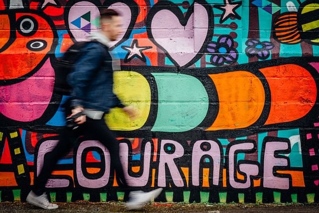 Man walking in front of a colorful mural with the word “courage” painted on it.